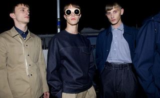 Three guys wearing E Tauts S/S 2015 collection. The guy on the left is wearing a navy shirt and brown jacket. Next to him the guy is wearing brown pants with denim shirt and sunglasses and on the right the guy is wearing a blue and white stripe shirt with denim jacket and denim pants