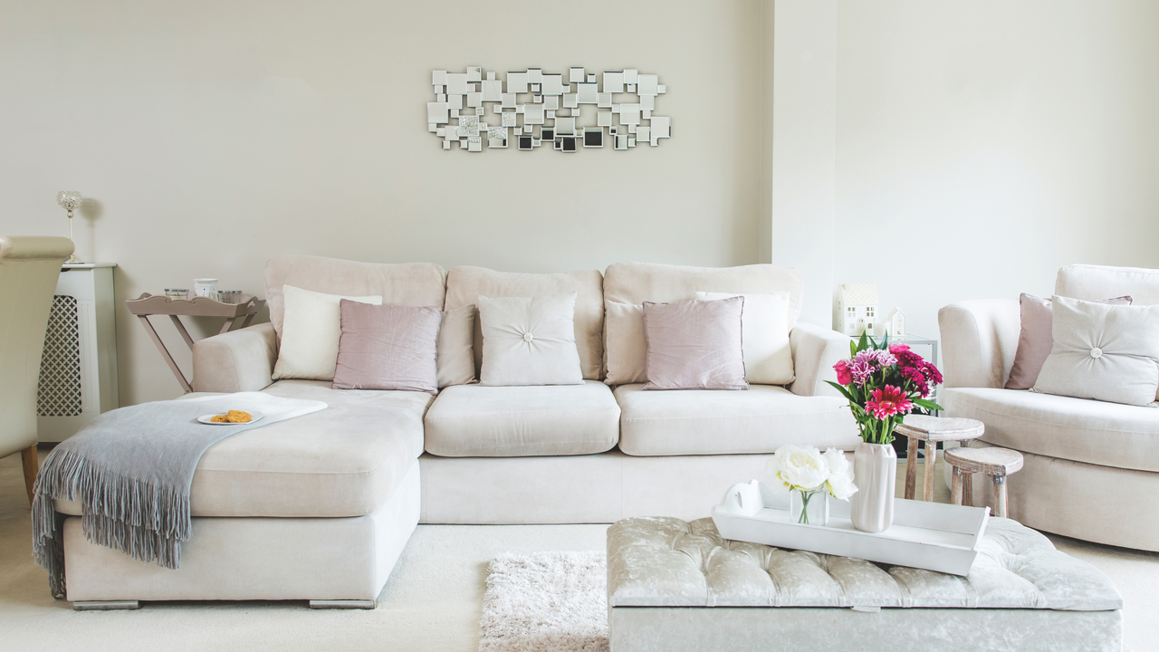 Living room with a large sofa and armchair, cushions and ottoman, a feature mirror and tray table and neutral decor.