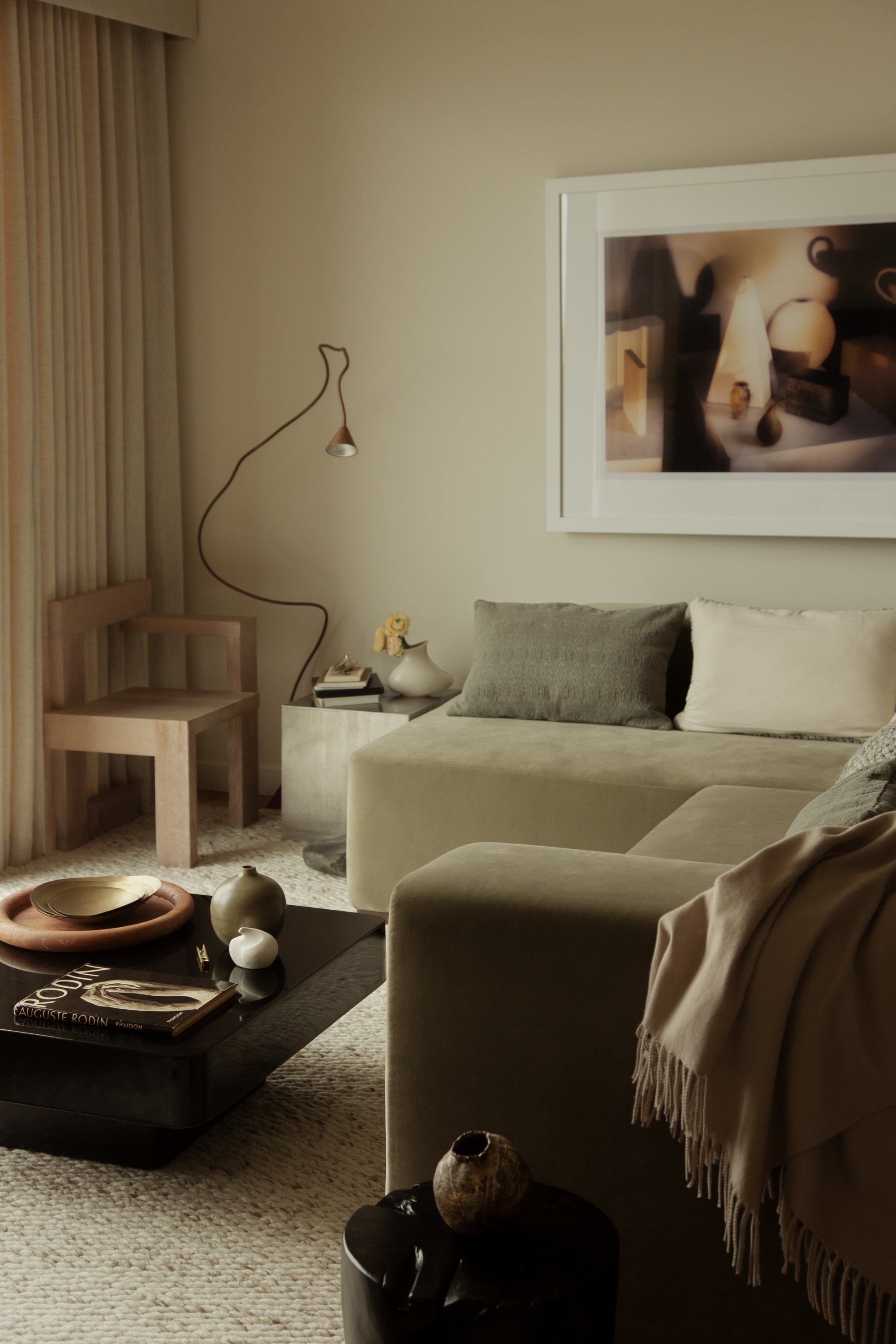 beige living room with beige sofa, artwork on wall, timber chair, and floor lamp, black square coffee table, and marle rug, with throw