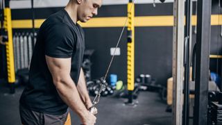 Man performs triceps press-down using cable machine