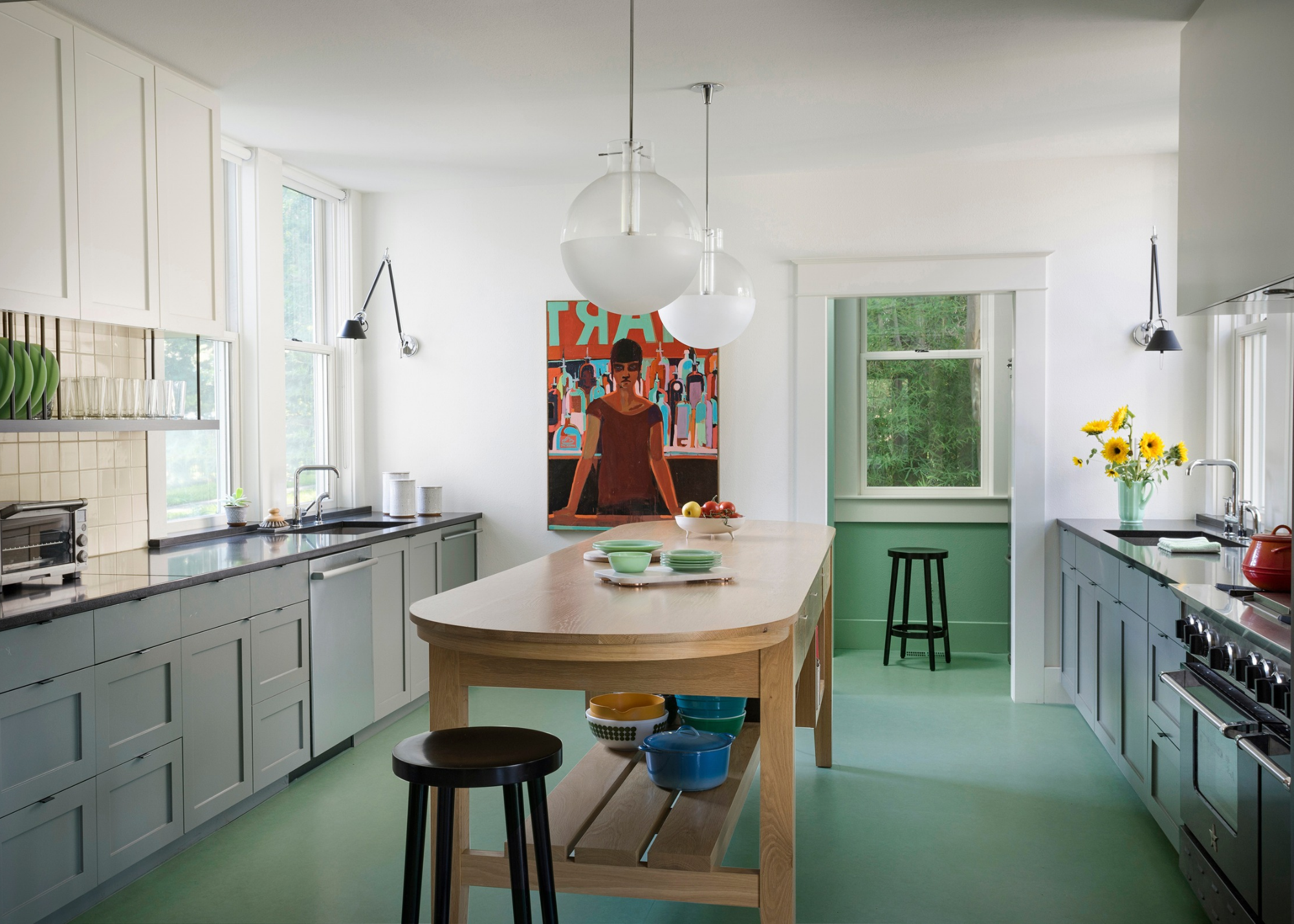 large kitchen with mint colored gloors, grey cabinets and a large wooden table in the centre