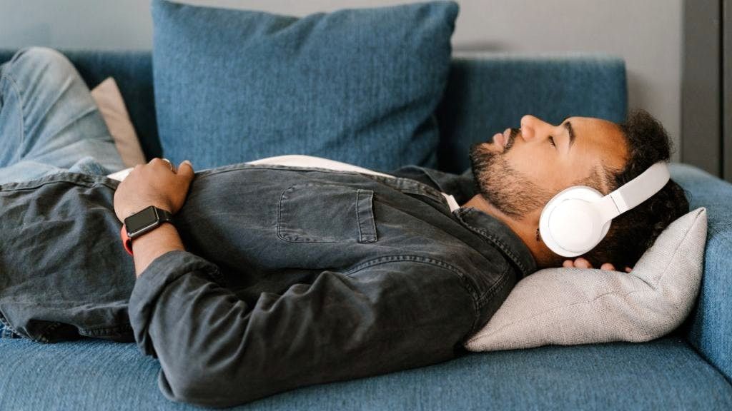 Man napping on sofa while wearing headphones