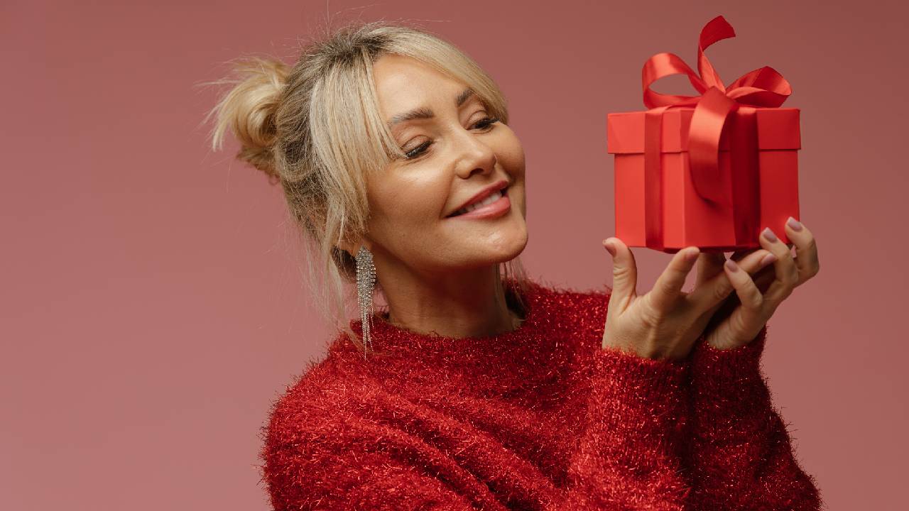 A happy woman wearing a sparkly red jumper while holding a small red present with a red bow.