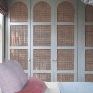 Bedroom with rattan built in wardrobes next to bed.