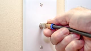 A person plugging a coaxial cable into the wall