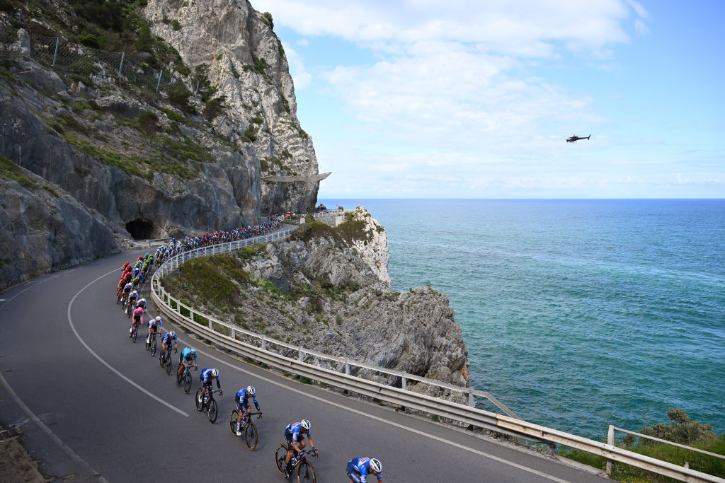 The peloton single file on a road overlooking the ocean