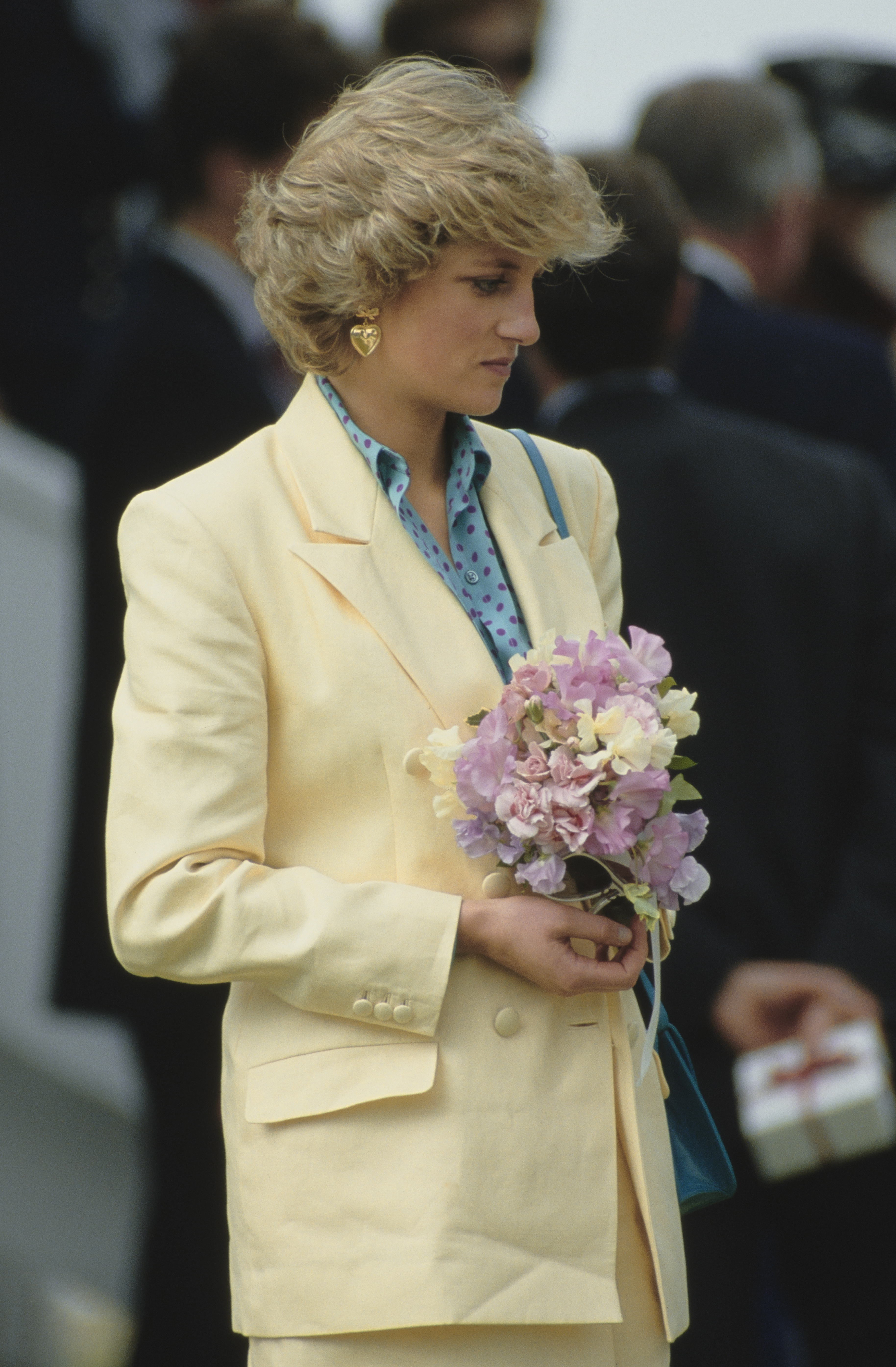 Princess Diana wearing a pale yellow blazer holding flowers