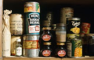 Close up of Marmite and tinned beans and fruit on wooden shelves in larder