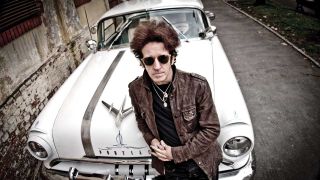 Willie Nile leaning on the hood of a classic Pontiac car