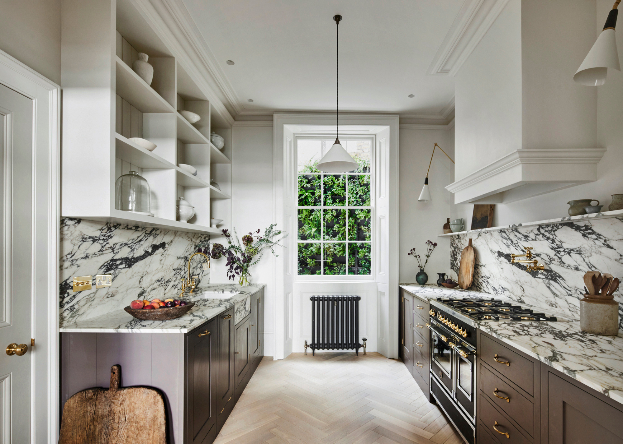 A large light galley kitchen with dramatically veined worktop, purple base units and off white wall units and a pendant light in the centre