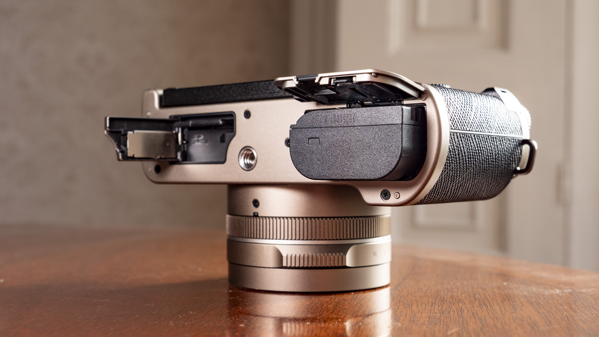 The underside of the Titanium Gold special edition of the Panasonic Lumix L10 compact camera, battery and memory card doors open, on an antique wooden table 