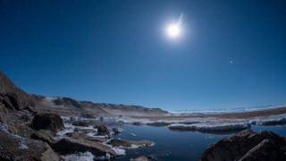 a very bright meteor lights up the dark sky above a tundra with snow and grass