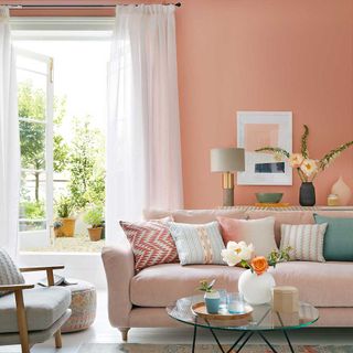 Peach walls in a living room with sheer curtains and a pink sofa