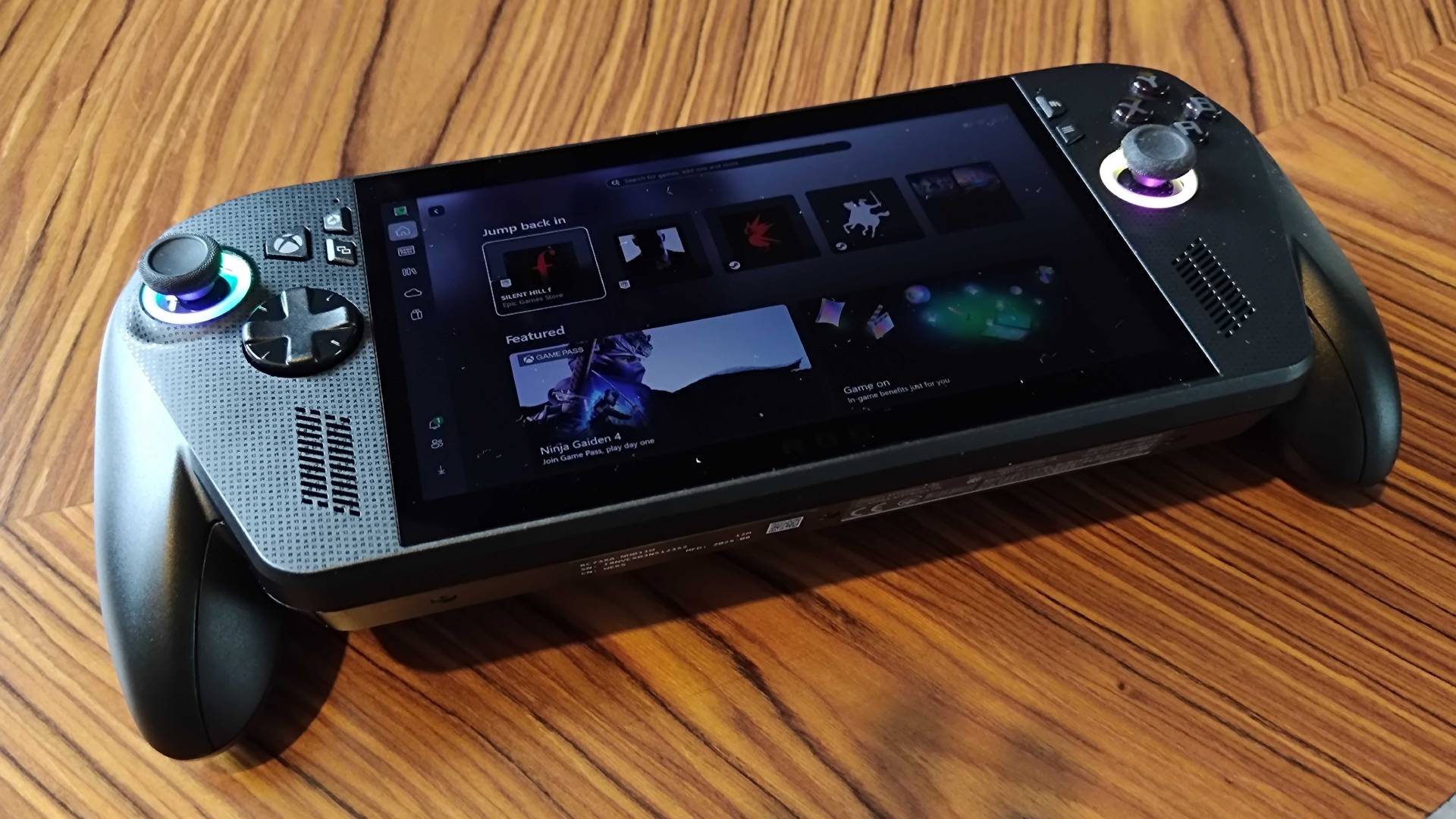 ROG Xbox Ally X handheld at an angle on woodgrain table.