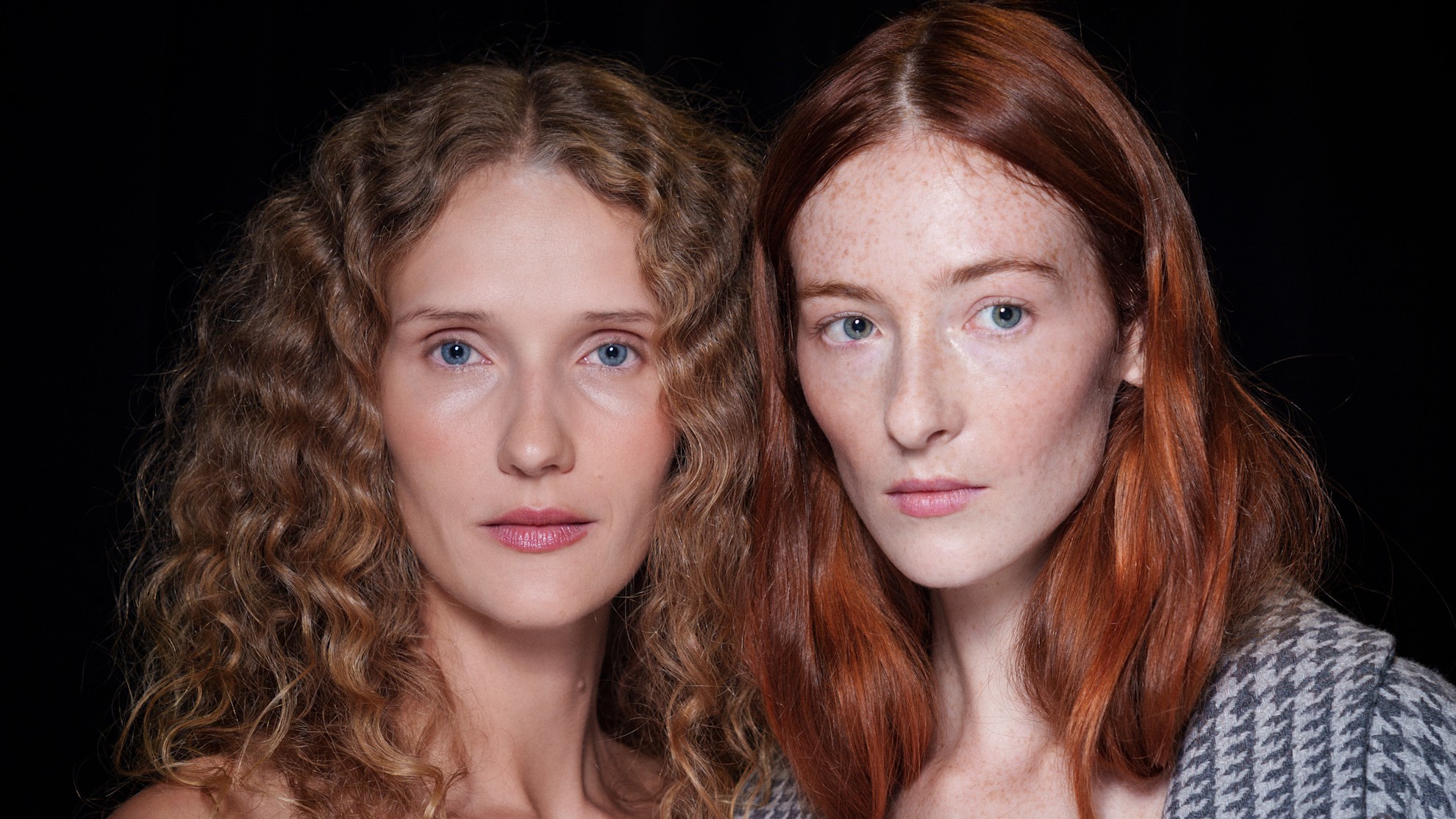 two pale models with blonde and red hair on a black background