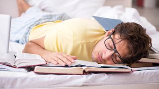 A college student who has fallen asleep on his bed while studying