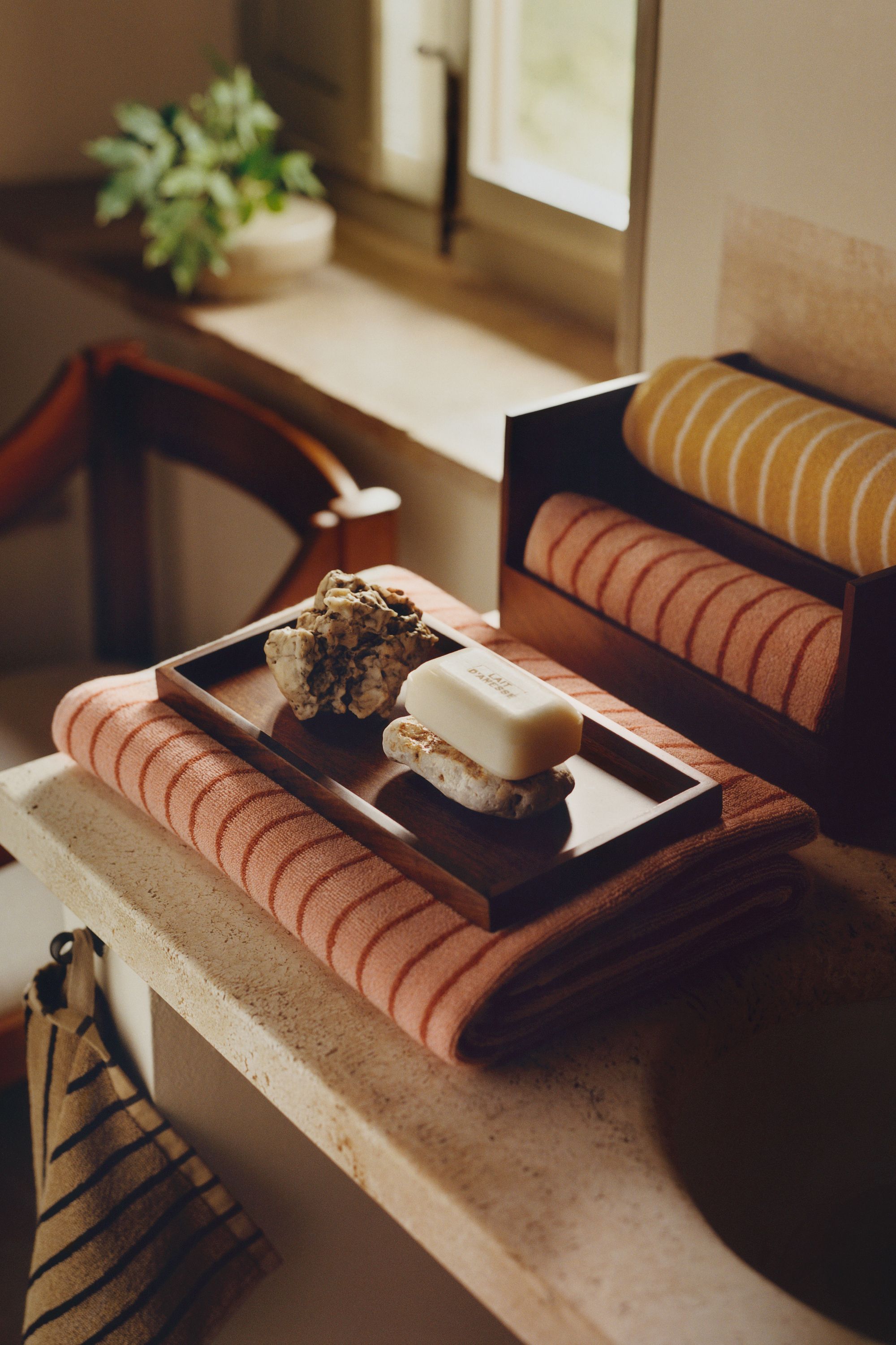 H&amp;M home striepd bath towels folded on countertop with tray and bar of soap with pummis stone