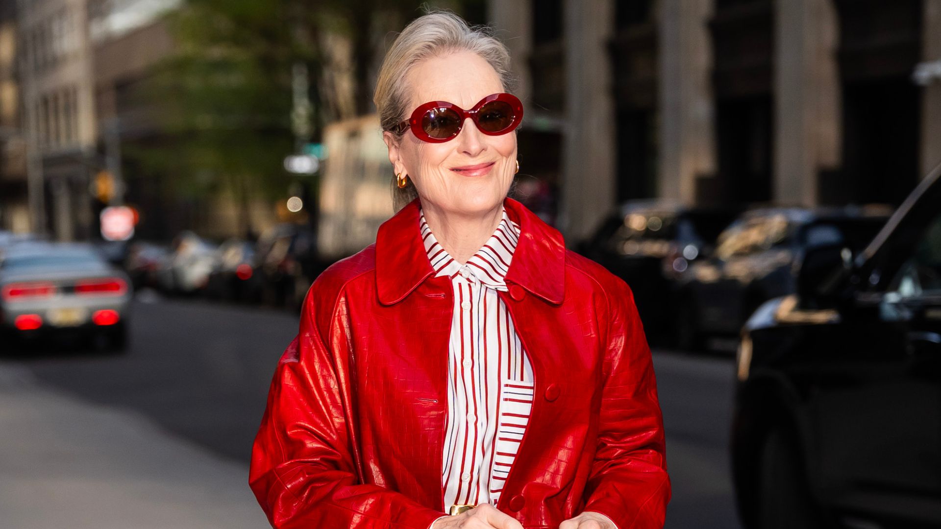 Meryl Streep steps outside in New York wearing a red leather coat with white jeans and red pointed-toe shoes and red sunglasses.