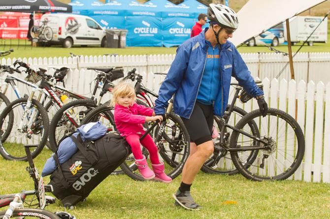 A rider pulls his daughter along to the bag drop area during the Prologue