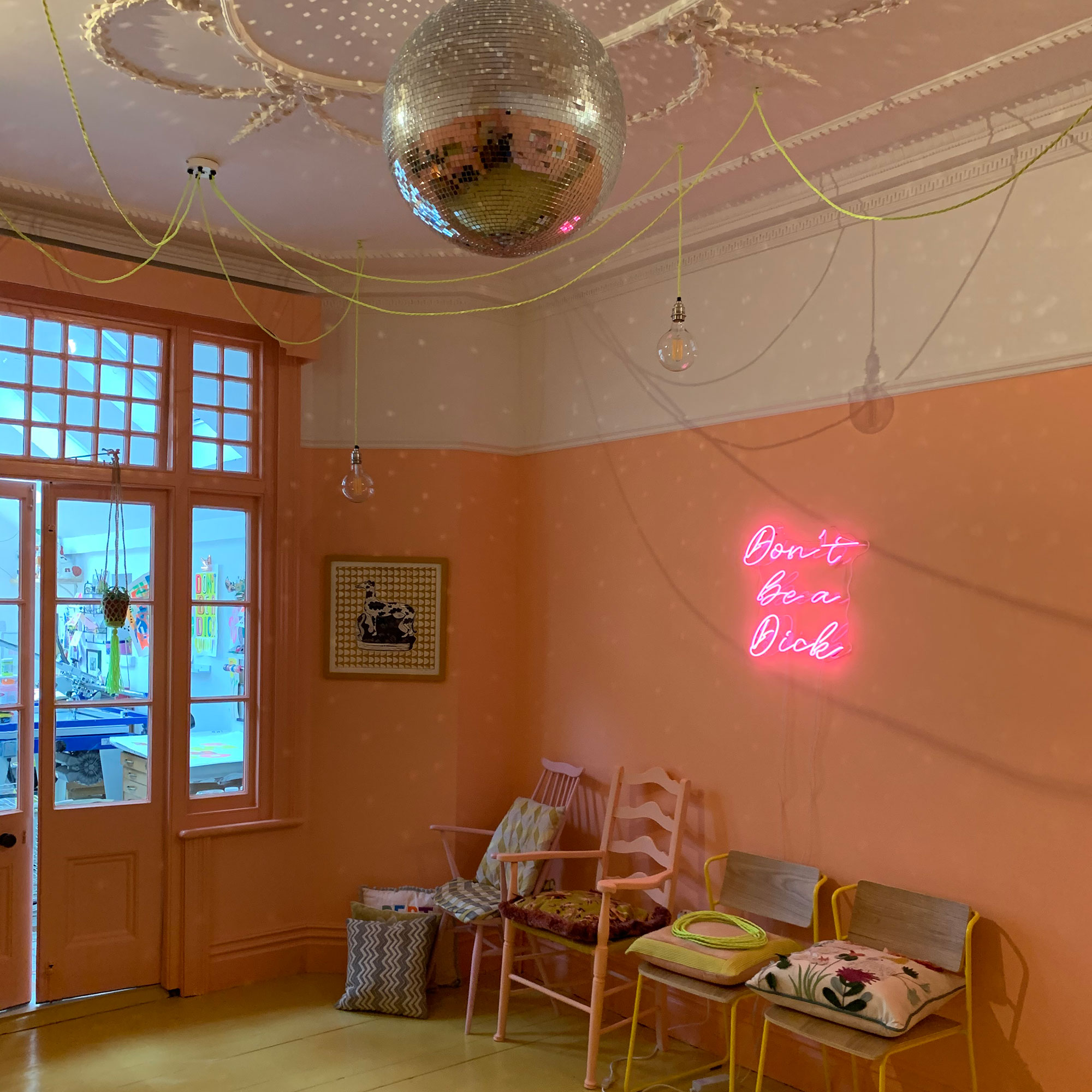 Entrance way painted peach with chairs against wall, neon artwork and mirror ball hanging from ceiling
