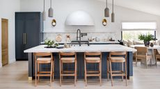 Blue kitchen and island with white countertop, oak bar stools and sculptural cooker hood