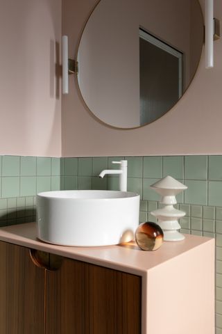 A bathroom tiled with sage green ceramic tiles and light pink wall paint