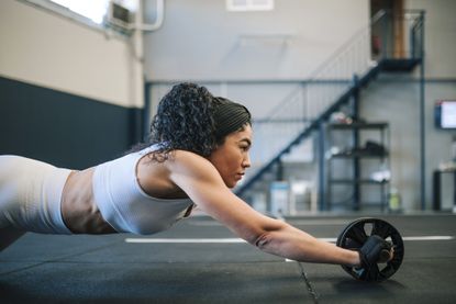 best ab roller: Pictured here, a fit athletic women using an ab roller in a large room