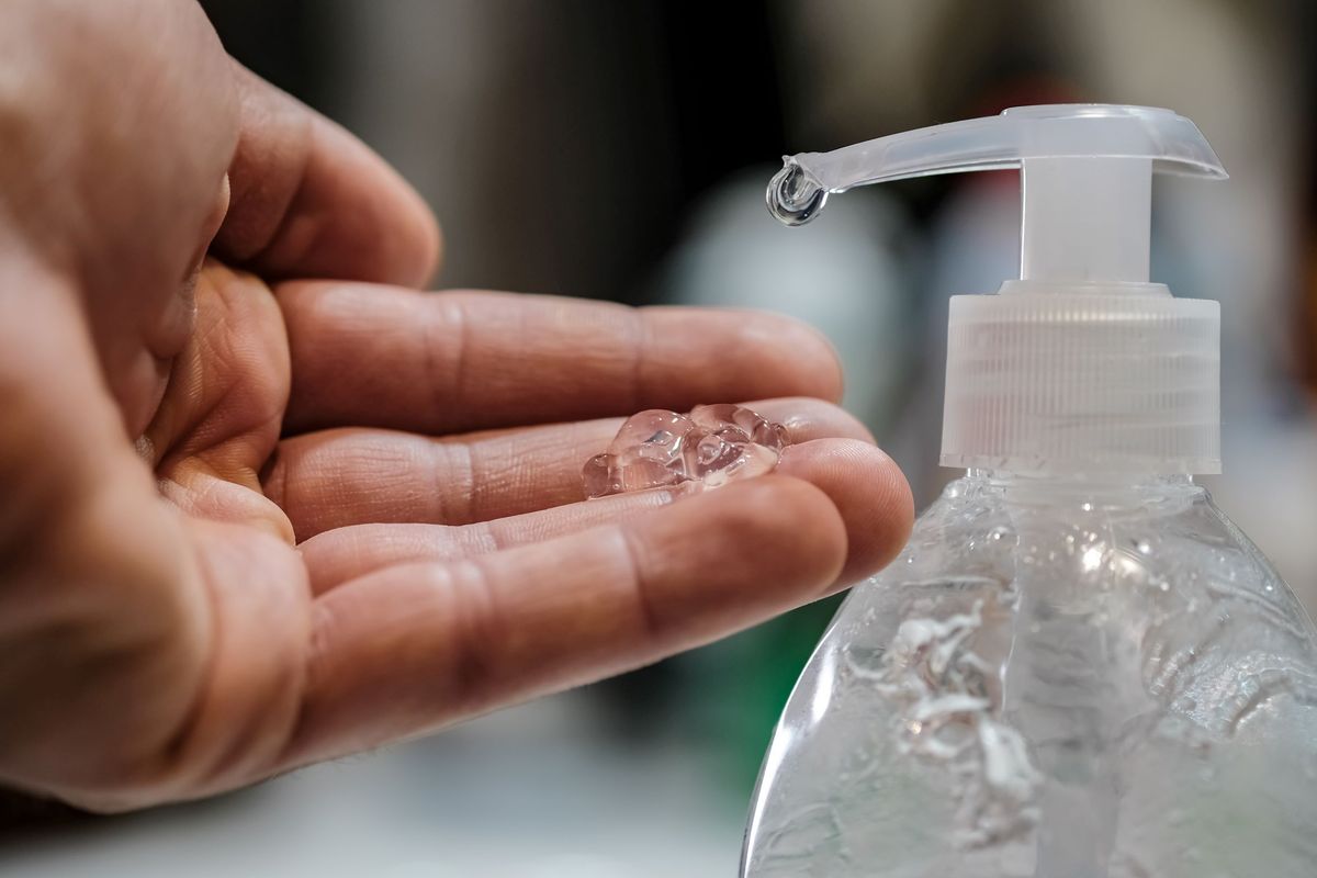 A person applying hand sanitizer to their hand from a bottle.