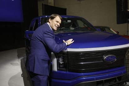 Ford CEO Jim Farley stands and smiles next to a Ford F-150 Lightning truck 
