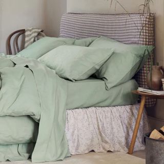 Sage green sheets on a mushroom gingham headboard against a cream wall.