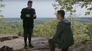 Dan Levy holding a ring box in front of Noah Reid on one knee on a hill on Schitt's Creek