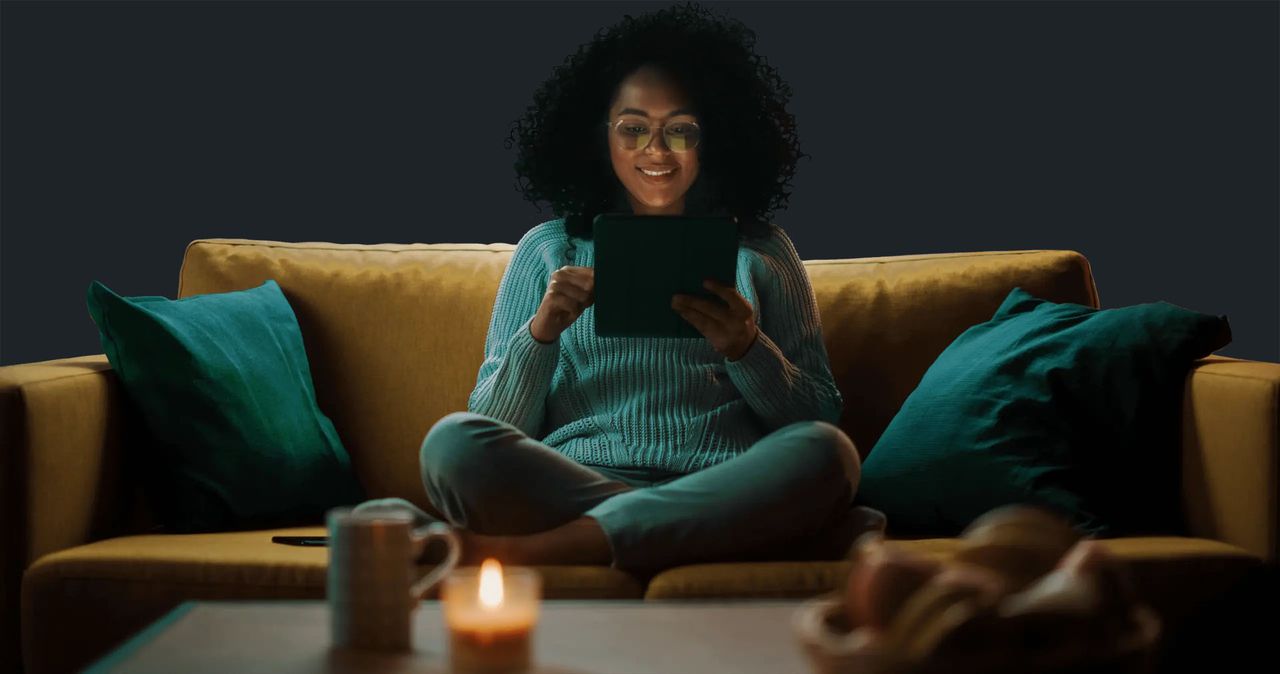 A woman sitting on a sofa reading an electronic tablet.
