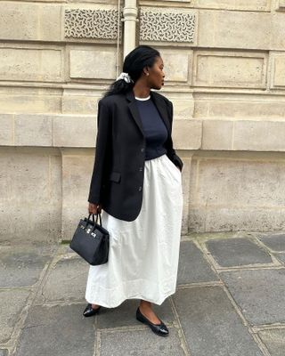 stylish woman in Europe wearing a black blazer, white skirt, and ballet flats