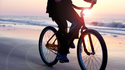 Silhouette of a person riding their bike on a tranquil beach at sunrise 