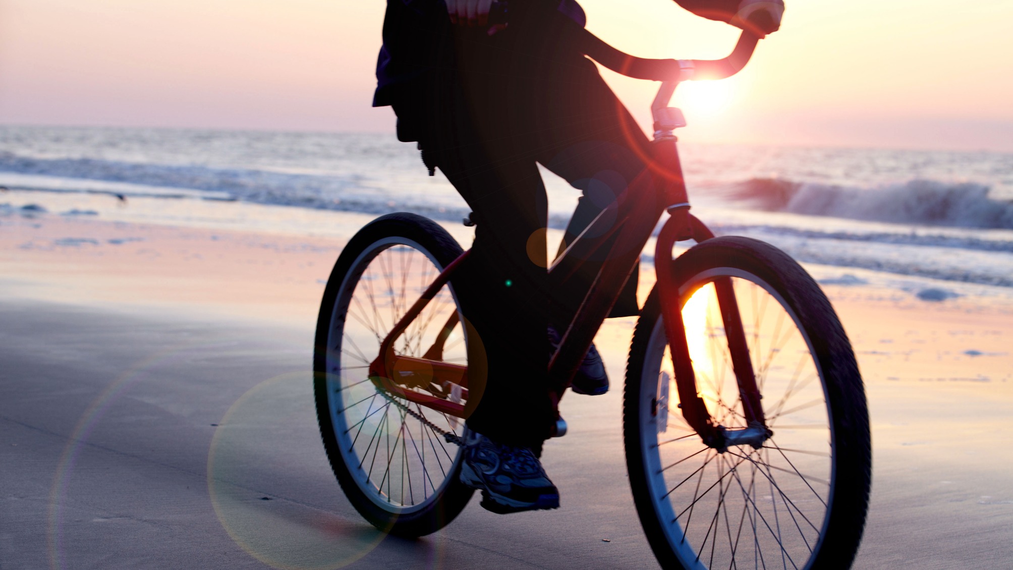 Silhouette of a person riding their bike on a tranquil beach at sunrise 