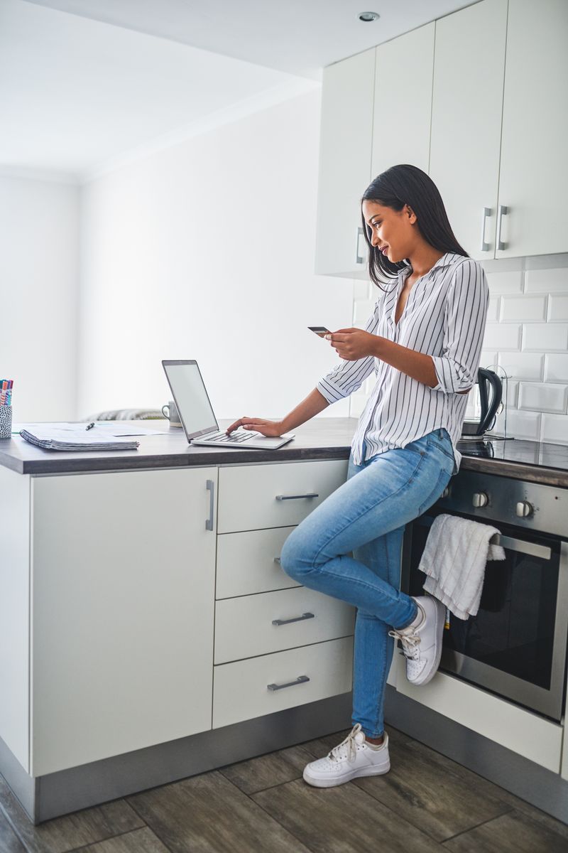 A woman stood at her laptop refers to a gift card in her hand