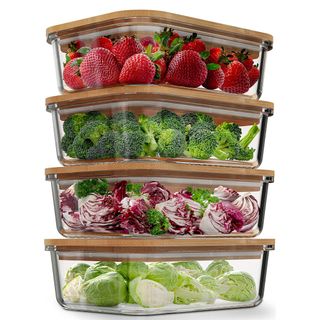 Four glass containers with bamboo lids hold sprouts, cabbage, broccoli, and strawberries