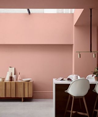 Pink painted basement kitchen, painted walls and ceiling, kitchen island with white and dark wood bar chairs, gray flooring, wooden sideboard in background