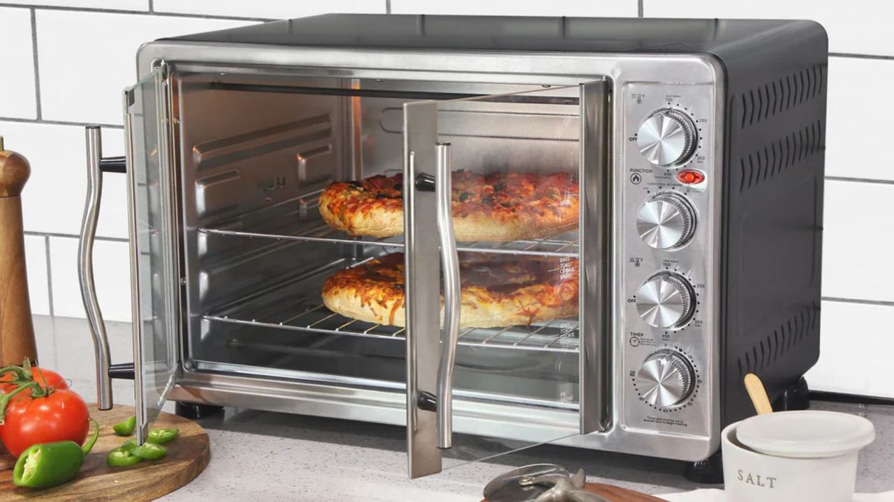 An Elite Gourmet French Door Convection Toaster Oven cooking two pizzas on a white kitchen countertop