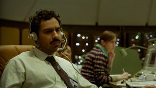 Kunal Nayyar's Peter sits at his space mission desk with a headset on in Netflix's Spaceman film
