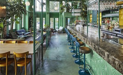 Bar and diner featuring marble bar top, leather stools, muted green walls and a range of plants