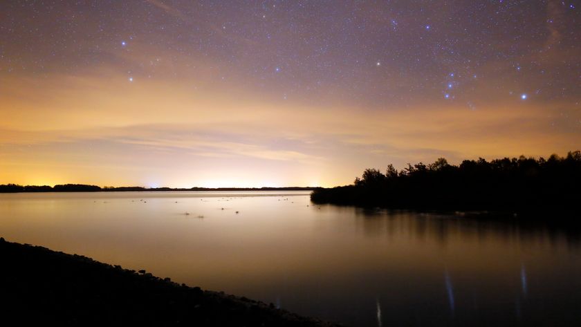 The constellation Orion is shown rising above a lake at sunset.