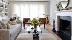 Bright white living room with large fireplace, sheer floor to ceiling curtains, built-in white bookshelves and hardwood floors