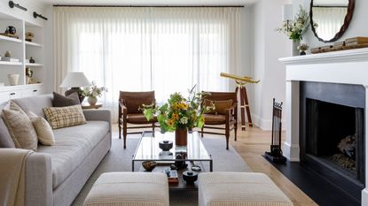 Bright white living room with large fireplace, sheer floor to ceiling curtains, built-in white bookshelves and hardwood floors