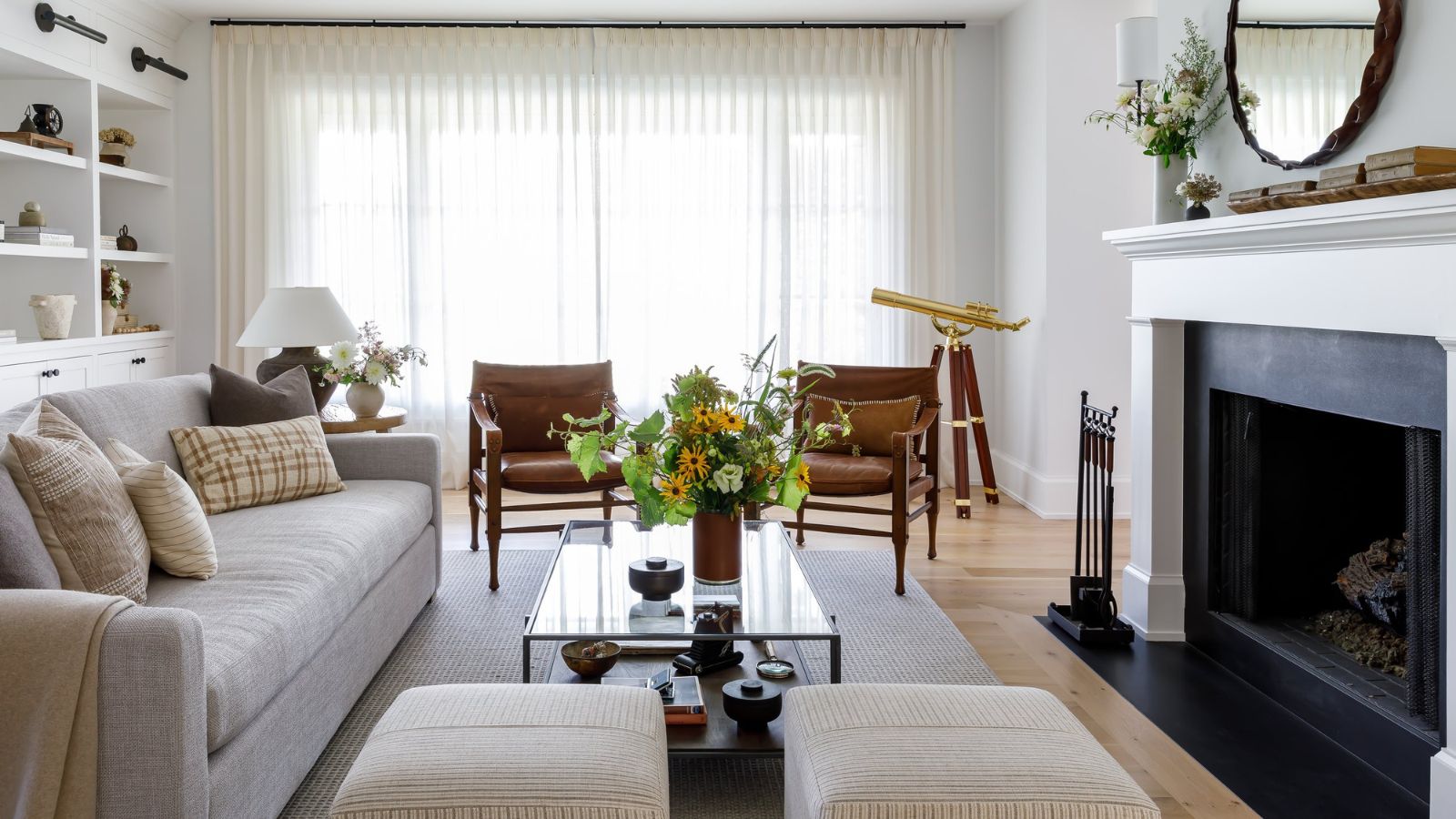 Bright white living room with large fireplace, sheer floor to ceiling curtains, built-in white bookshelves and hardwood floors