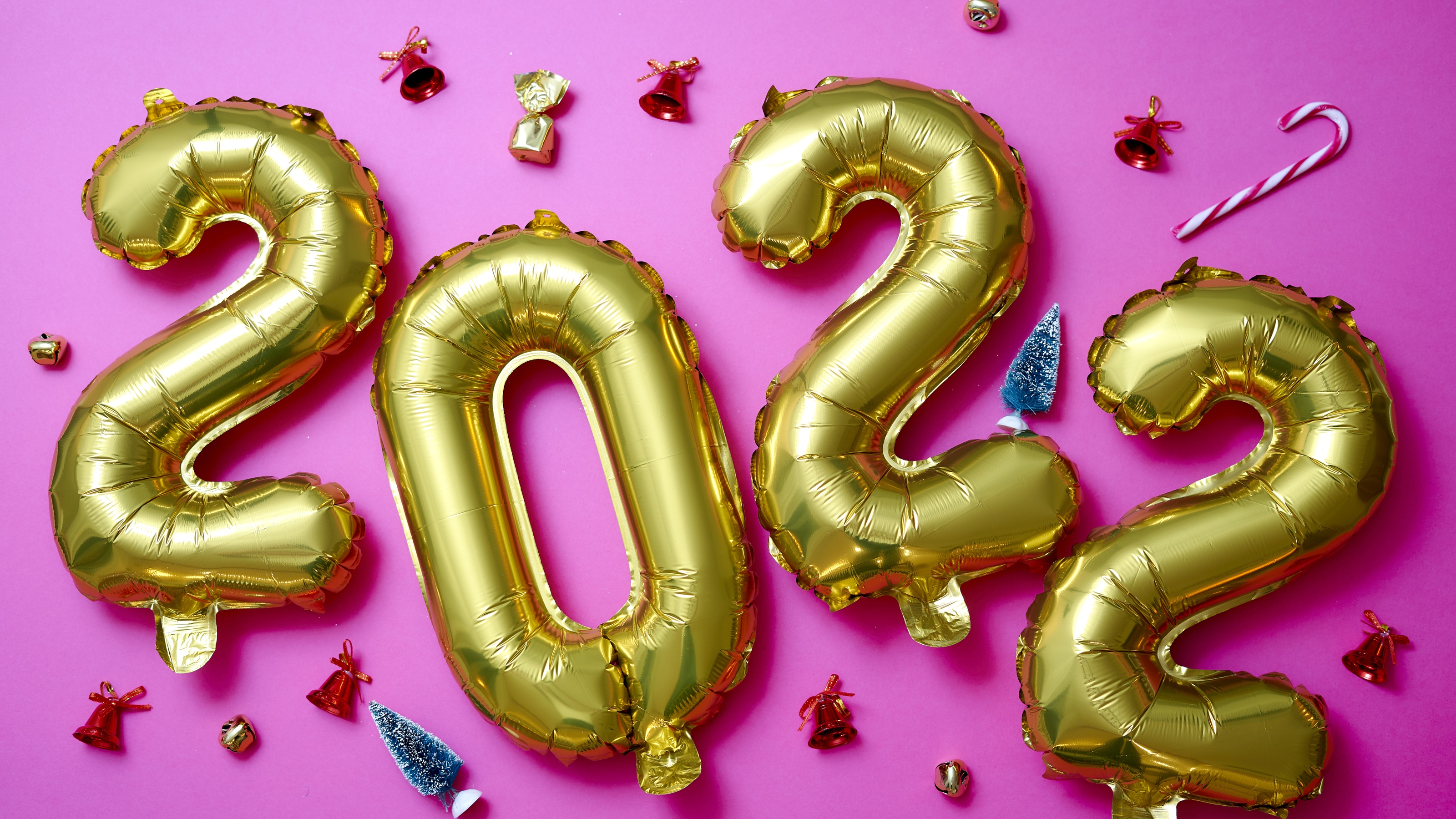 Gold balloons spell out 2022 against a pink background and party favors.