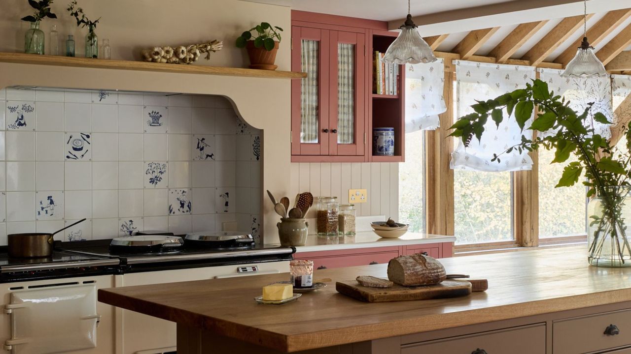 beautiful farmhouse kitchen with soft beige walls, earthy pink cabinets, a large island, and large range cooker tiled with vintage delft tile backsplash