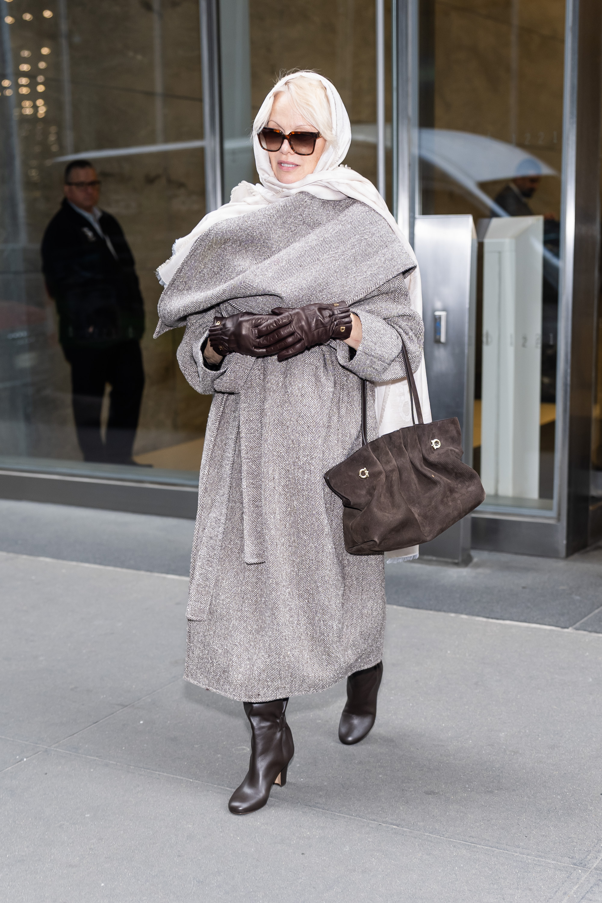 Pamela Anderson styled a herringbone wrap coat with a Ferragamo suede bag, matching boots and globes, plus a hair scarf