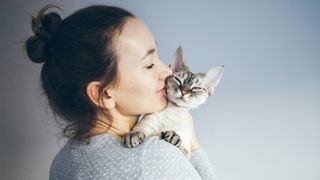 Devon rex cat sitting on woman's shoulder as she nuzzles its face