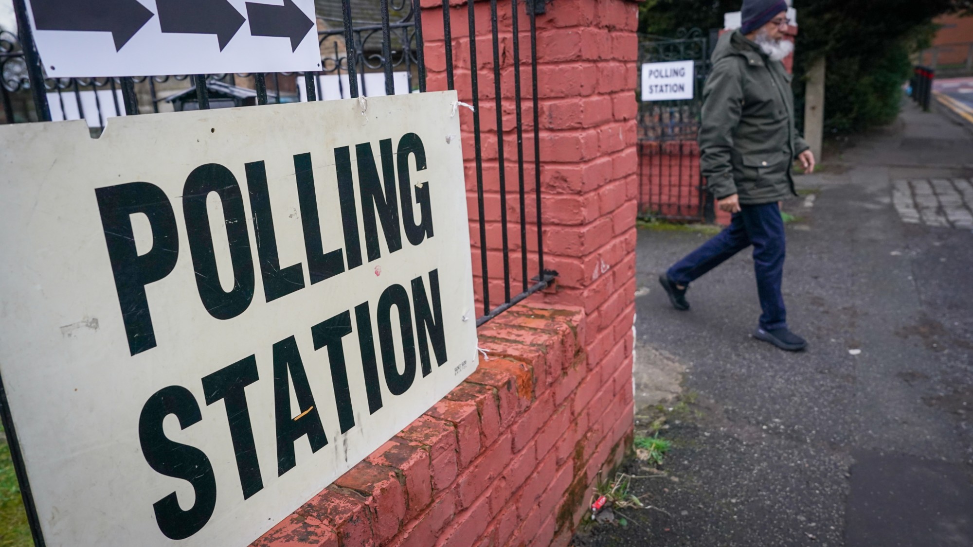 Man walks out of polling station in Gorton and Denton, behind sign saying "polling station"